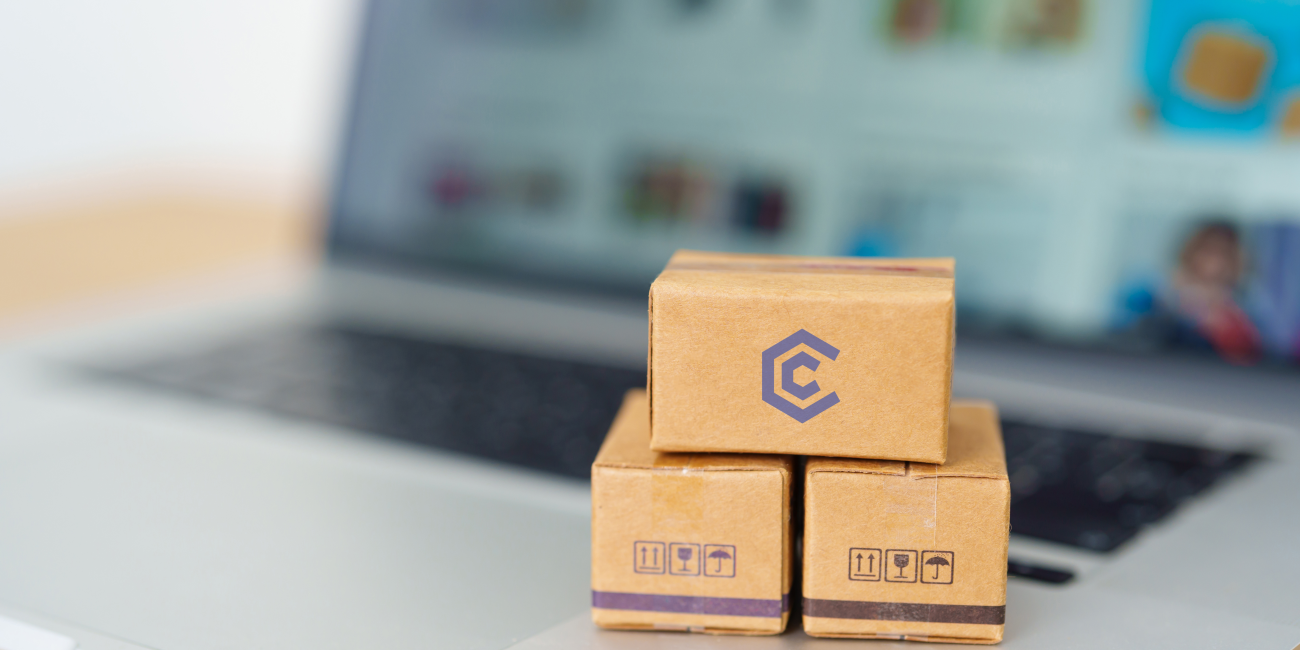 Cardboard boxes with a click computer logo stacked in front of a laptop, symbolizing online shopping at the best online PC shop in South Africa.