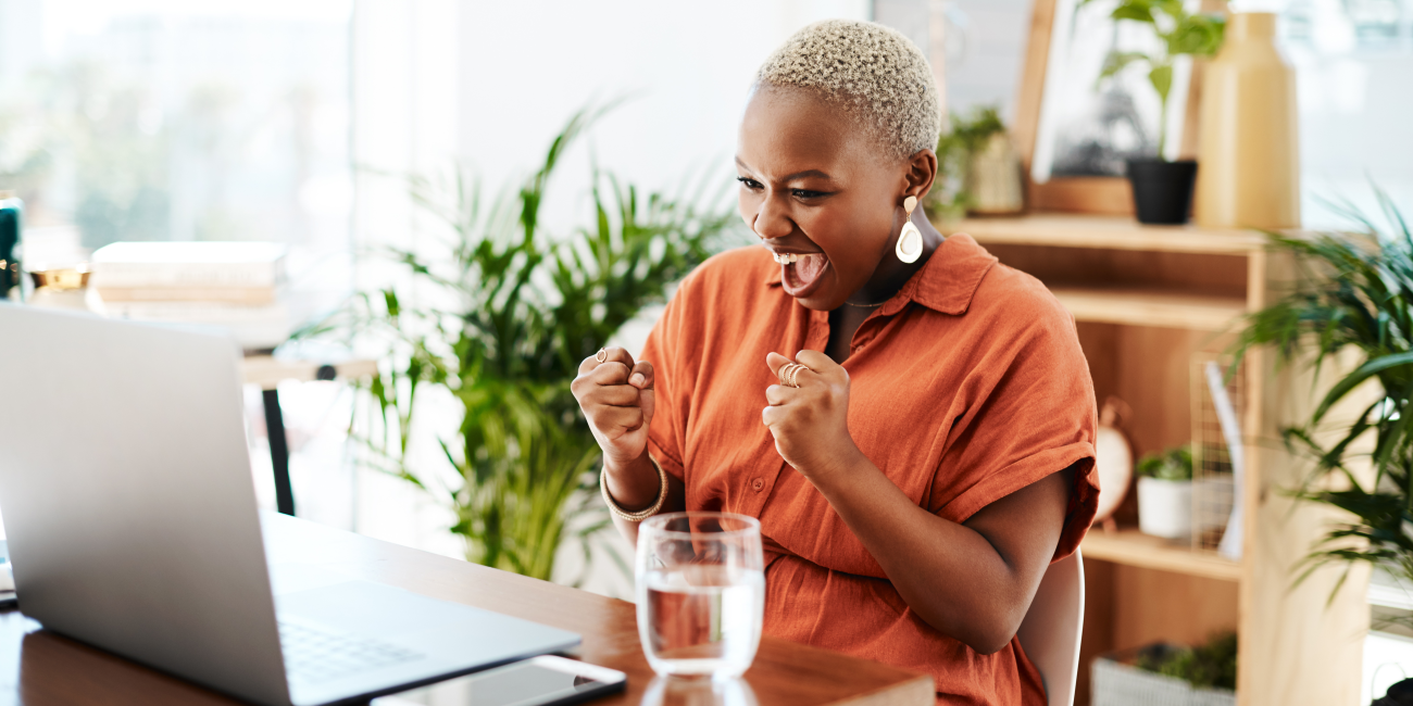 A woman excitedly celebrates while working on her laptop, showcasing the joy of finding the best computer price deals online.
